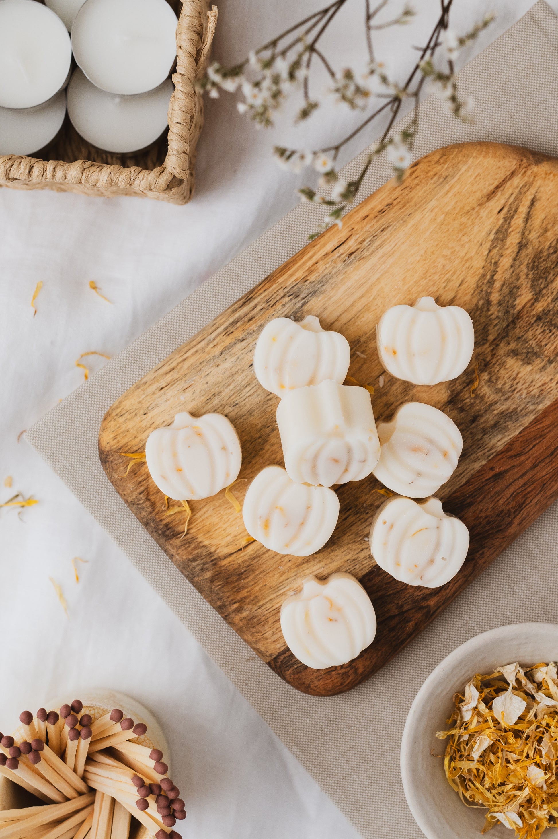 Pumpkin-shaped botanical soy wax melts displayed on a chopping board. Tealights, petals and matches to decorate.